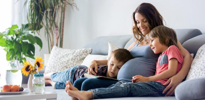 Young pregnant woman, reading a book at home to her two boys