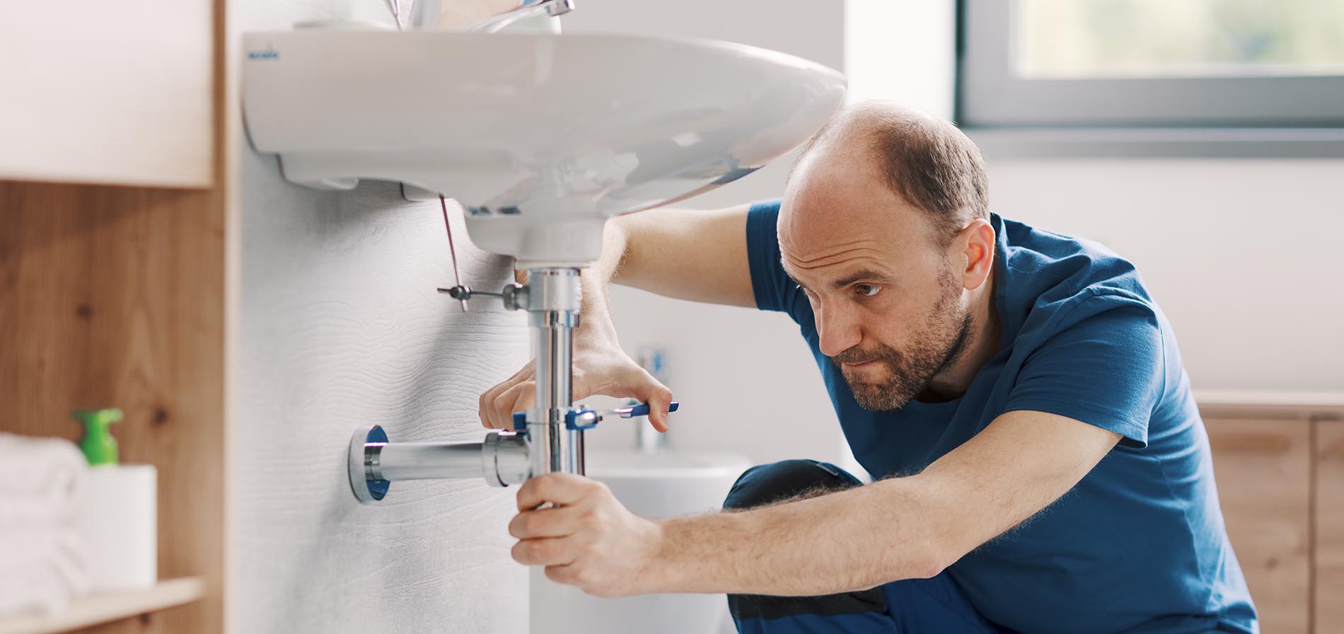 Expert plumber working on a bathroom sink drain, he is using water pump pliers and fixing a pipe